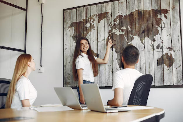 Three people in a meeting, one presenting with a world map on the wall behind - Domestic and Overseas Recruitment